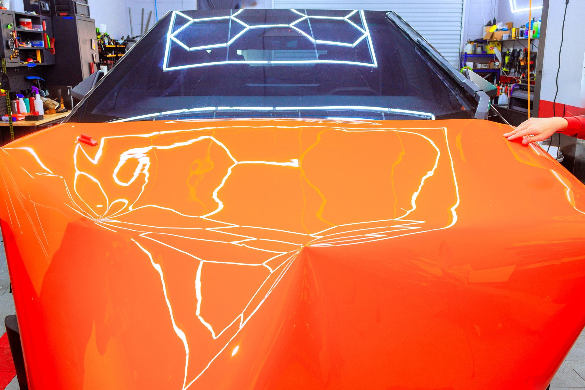 Bright orange car hood being polished in a well-lit automotive workshop with tools nearby